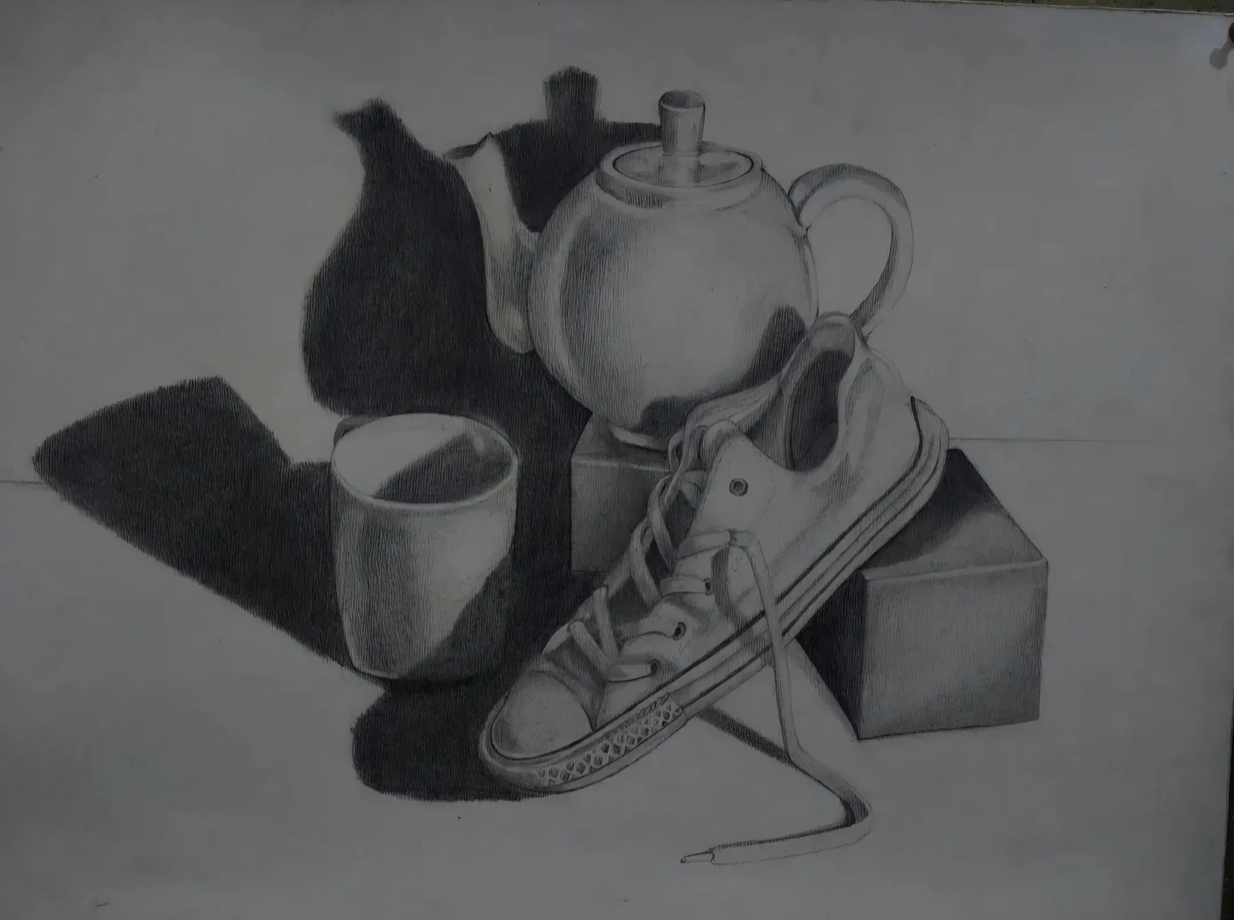 Graphite still life of a teapot, mug, box, and a sneaker with cast shadows